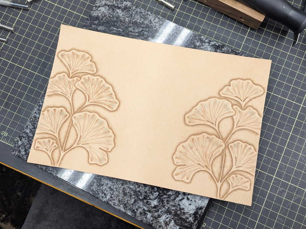Work in progress of tooling ginkgo leaves on a natural leather cover on a quartz slab