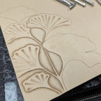 Work in progress of tooling ginkgo leaves on a natural leather cover on a quartz slab