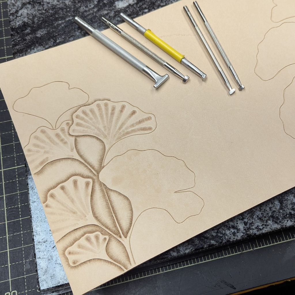 Work in progress of tooling ginkgo leaves on a natural leather cover with carving tools on a quartz slab