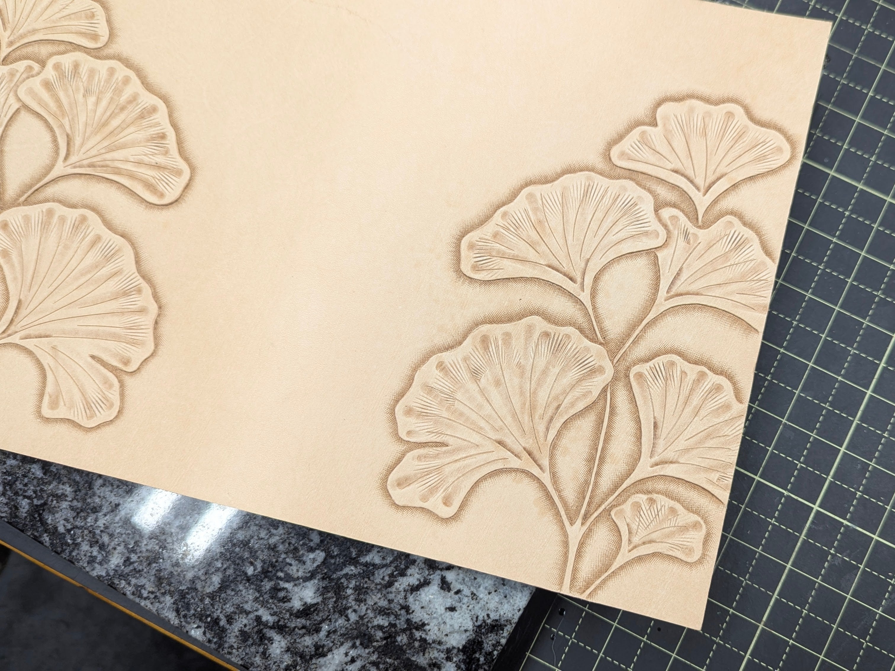 Work in progress of tooling ginkgo leaves on a natural leather cover on a quartz slab