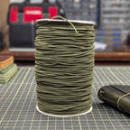 Spool of green thread on a grid surface with tools in the background