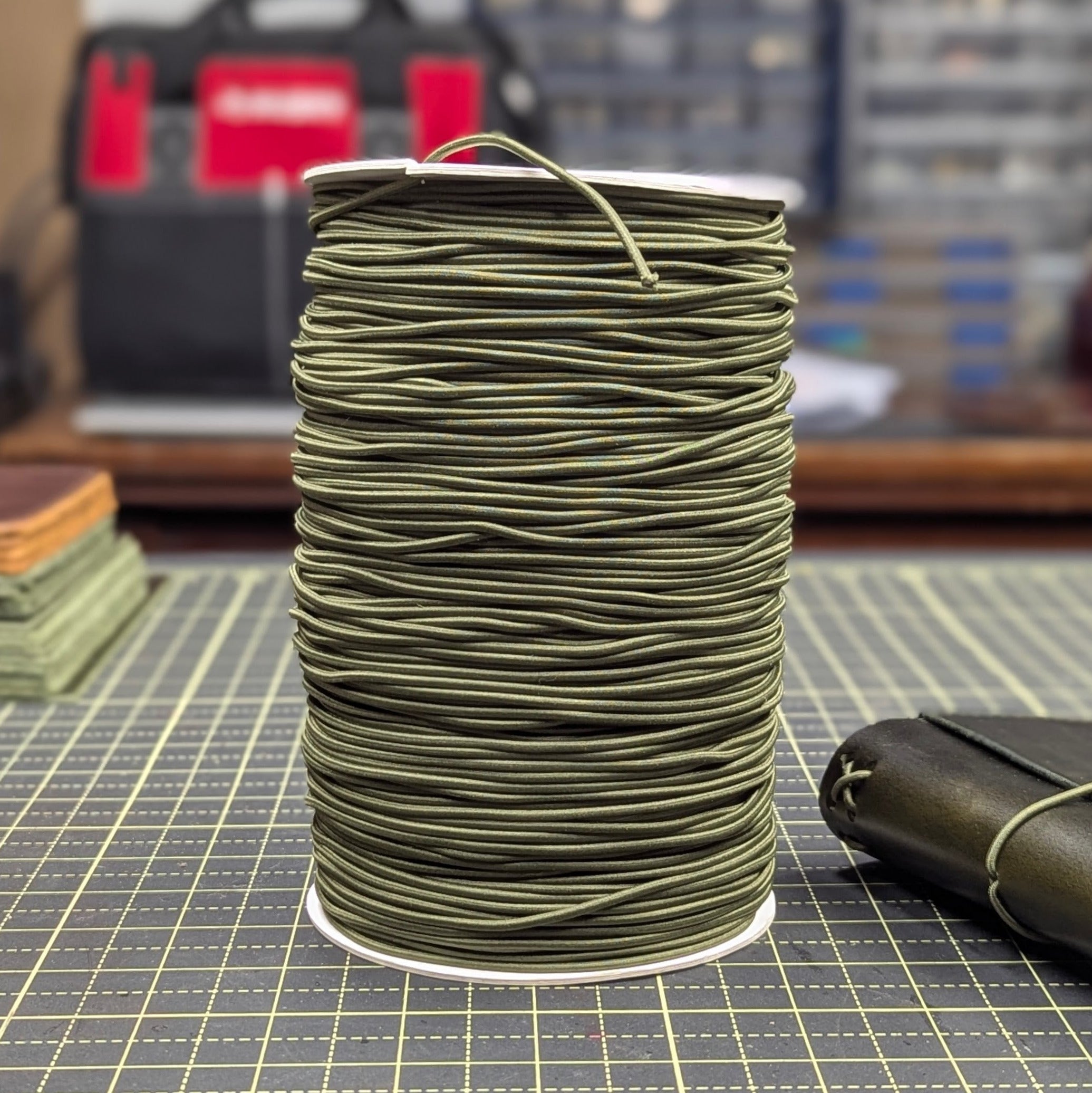 Spool of green thread on a grid surface with tools in the background