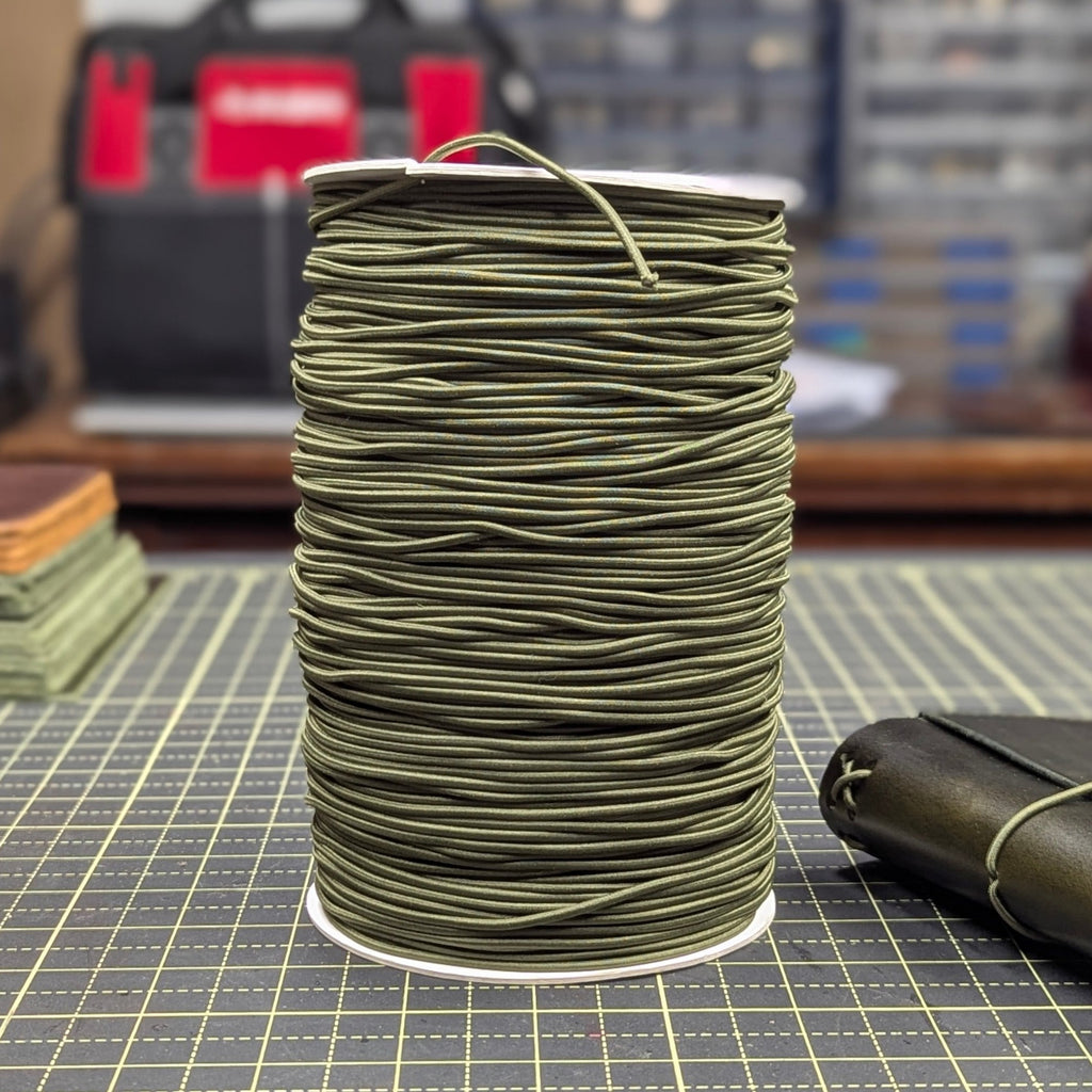 Spool of green thread on a grid surface with tools in the background