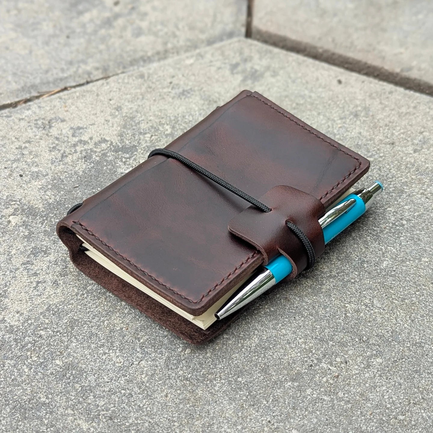Brown leather notebook with blue pen on a concrete surface