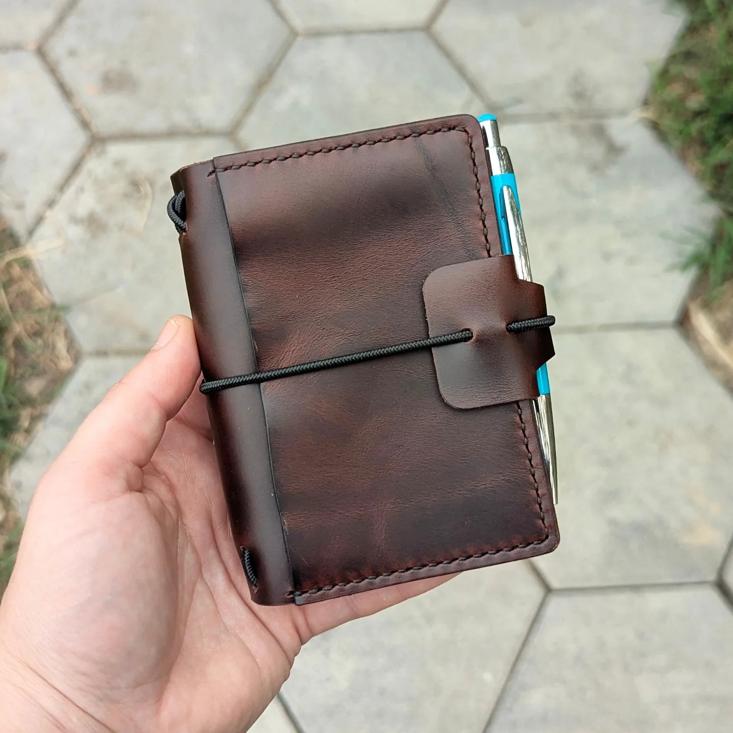Brown leather notebook held in a hand with a blurred outdoor background