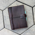 Brown leather notebook with pen holder on a textured surface