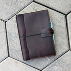 Brown leather notebook with pen holder on a textured surface