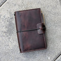 Brown leather notebook with pen holder on a gray pavement