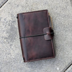 Brown leather notebook with pen holder on a gray pavement