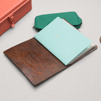 Brown leather notebook cover open holding three notebook inserts with pencil case and toolbox staged around